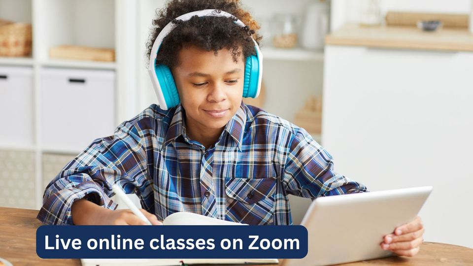 A boy in headphones working in his exercise book beside his laptop during a live online class