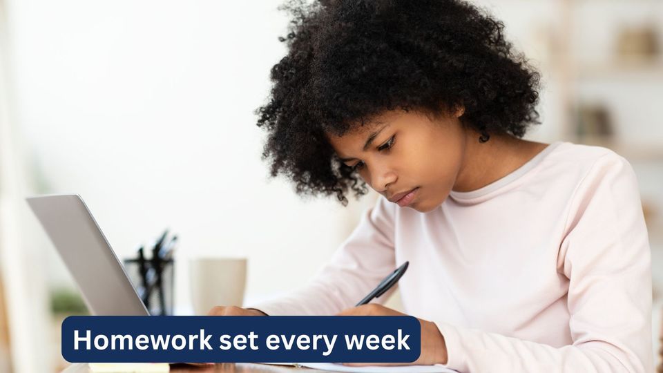 A girl doing her weekly homework by hand beside her laptop